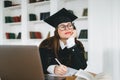 Young pensive caucasian woman college student in graduation outfit , sitting in front laptop with books and thinking about future Royalty Free Stock Photo