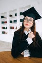 Young pensive caucasian woman college student in graduation outfit , sitting in front laptop with books and thinking about future Royalty Free Stock Photo