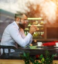 Young pensive dreamy male businessman meditating thoughtfully in cafe view through window with reflections on glass