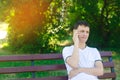A young pensive European guy in a white T-shirt speaks on the phone and sits on a bench in the city park. The concept of solving p Royalty Free Stock Photo
