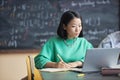 Young pensive female student in green pullover looking at laptop screen Royalty Free Stock Photo