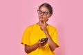 Young pensive Indian woman student uses smartphone stands in pink studio Royalty Free Stock Photo