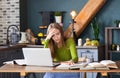 Young pensive woman freelancer sitting at table at home with laptop, making notes Royalty Free Stock Photo