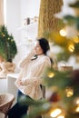Young pensive woman stands in kitchen against background of Christmas tree