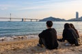 Young people at the bech looking at the horizon. Group of friends talking. Dressed in black. Korean youth. Long Gwangan bridge