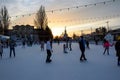 Young people of different ages and genders have a fun and active time, skating on the ice rink in the evening city square