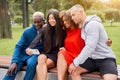 Young people of different nationalities take selfies using smartphones, sitting on a bench in the park in summer. Athletic build.