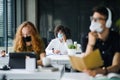 Young people with face masks back at work or school in office after lockdown.