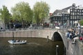 Young people sit on bridge over amsterdam canal while small boat Royalty Free Stock Photo