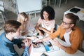 Young people sitting in office and happily looking at each other while discussion something. Group of cool guys working