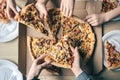 Young people taking slices of hot pizza from cardboard box at table, top view. Royalty Free Stock Photo