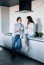 Attractive young woman and handsome man are enjoying spending time together while standing on light modern kitchen with cup of Royalty Free Stock Photo