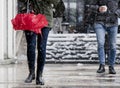 Young people walking on snowy winter city sidewalk, holding umbrella and warm drink