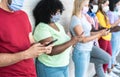 Young people wearing face safety masks using smart mobile phones while keeping social distance during coronavirus time -