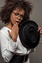 Young perplexed african american woman in white shirt wearing glasses and holding hat