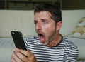 Young perplexed and shocked man using mobile phone looking internet social media or checking news in surprised and crazy disbelief