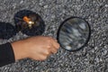 A young person burns tree leaves with a magnifying glass.