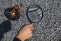 A young person burns tree leaves with a magnifying glass.