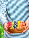 A young person holding up a large bowl of fresh berries and frui