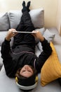 Young person lying down with headphones using a tablet on the sofa.