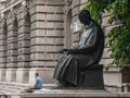 Young person, a man, sitting in front of a statue of the scientist Nikola Tesla wearing face mask protective equipment