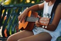 young person strumming a ukulele while seated on a bench