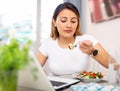 Peruvian housewoman eating salad and watching movie on laptop