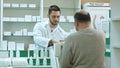 Young pharmacist giving drug to senior man customer and taking payment in dollars at drugstore