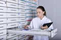 Beautiful young pharmacist standing next to medicine shelves, holding tablet