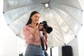 Young photographer lady working with professional camera in front of reflective umbrella in modern photostudio Royalty Free Stock Photo