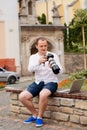 Young photographer with laptopon stone bench andtaking photo on camera