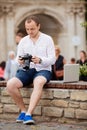 Young photographer with laptopon stone bench andtaking photo on camera