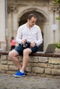 Young photographer with laptopon stone bench andtaking photo on camera