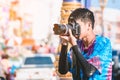 A young photographer in wet clothes use DSLR camera to take pictures of Songkran water splashing festival on the road
