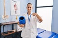 Young physiotherapist woman holding foam roll at the clinic pointing finger to one self smiling happy and proud