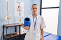 Young physiotherapist woman holding foam roll at the clinic thinking attitude and sober expression looking self confident