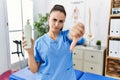 Young physiotherapist woman holding massage body lotion with angry face, negative sign showing dislike with thumbs down, rejection