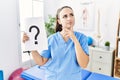 Young physiotherapist woman holding question mark serious face thinking about question with hand on chin, thoughtful about Royalty Free Stock Photo
