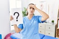 Young physiotherapist woman holding question mark stressed and frustrated with hand on head, surprised and angry face Royalty Free Stock Photo
