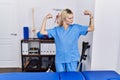 Young physiotherapist woman working at pain recovery clinic showing arms muscles smiling proud Royalty Free Stock Photo