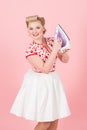 Young pin-up styled girl holds iron on pink background. Royalty Free Stock Photo