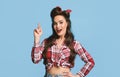 Young pinup lady in retro clothes pointing upwards on blue studio background