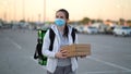 Young pizza courier is delivering an order. Delivery woman holding cardboard boxes in medical mask