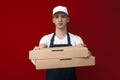 Young pizza delivery man in uniform on a red background gives a ready order, the courier guy holds pizza boxes Royalty Free Stock Photo