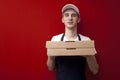 Young pizza delivery man in uniform on a red background gives a ready order, the courier guy holds pizza boxes Royalty Free Stock Photo