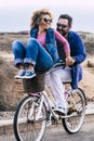 Young playful adult couple man and woman have fun together in outdoor leisure activity riding a single bike and laughing a lot - Royalty Free Stock Photo