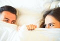 Young playful couple having fun in the bed - Happy lovers looking shy at each other in eyes lying under sheets in the bedroom Royalty Free Stock Photo