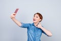Young playful girl is making selfie on the camera of her telephone and showing like sign Royalty Free Stock Photo