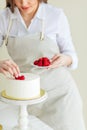 Young pleasant woman putting berries on the top of the cake