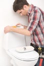 Young plumber repairing flush toilet. Royalty Free Stock Photo